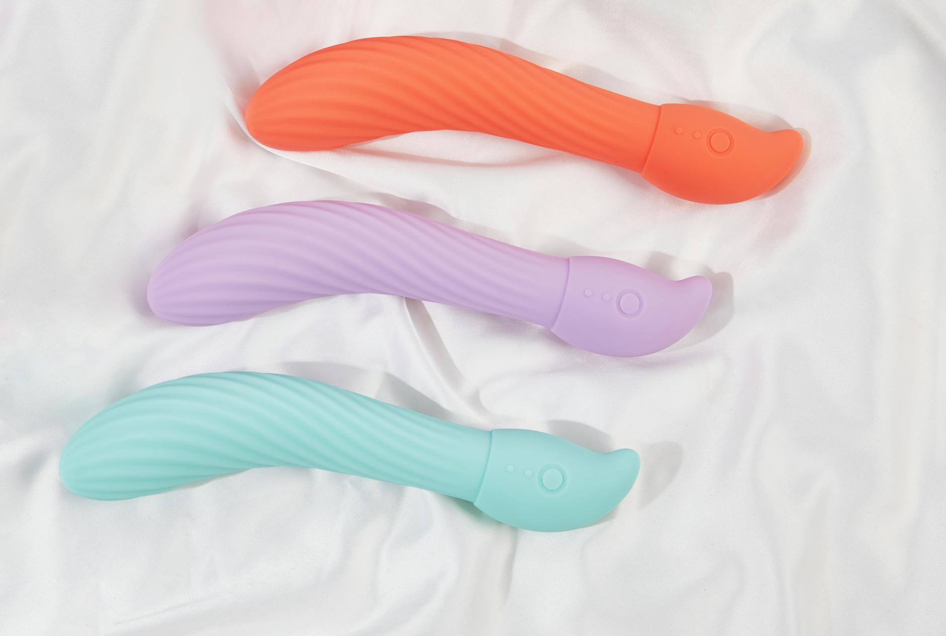 Trois vibromasseurs colorés arrangés sur du tissu blanc, soulignant leur texture lisse et leur design moderne.