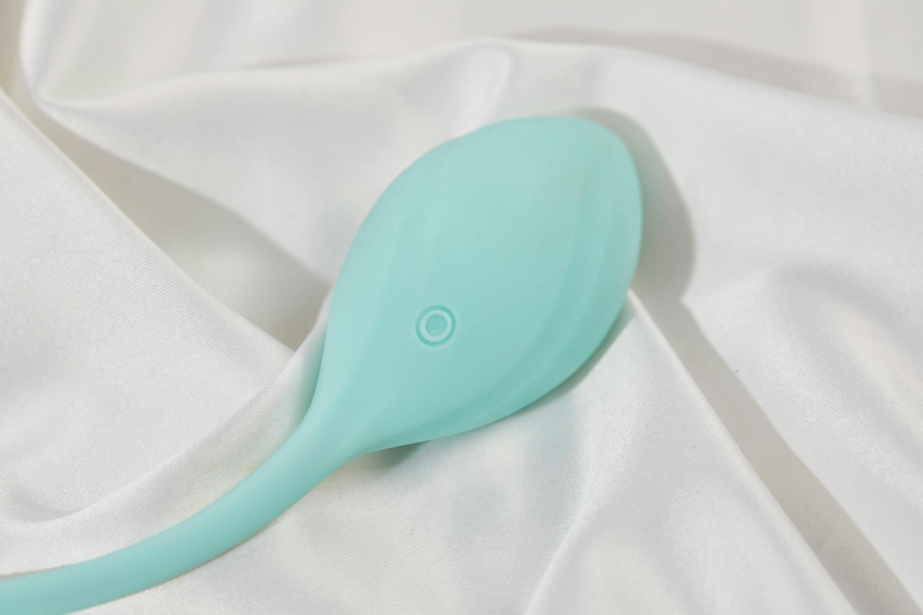 A stylish teal vibrator on smooth white silk fabric, representing sensual self-care