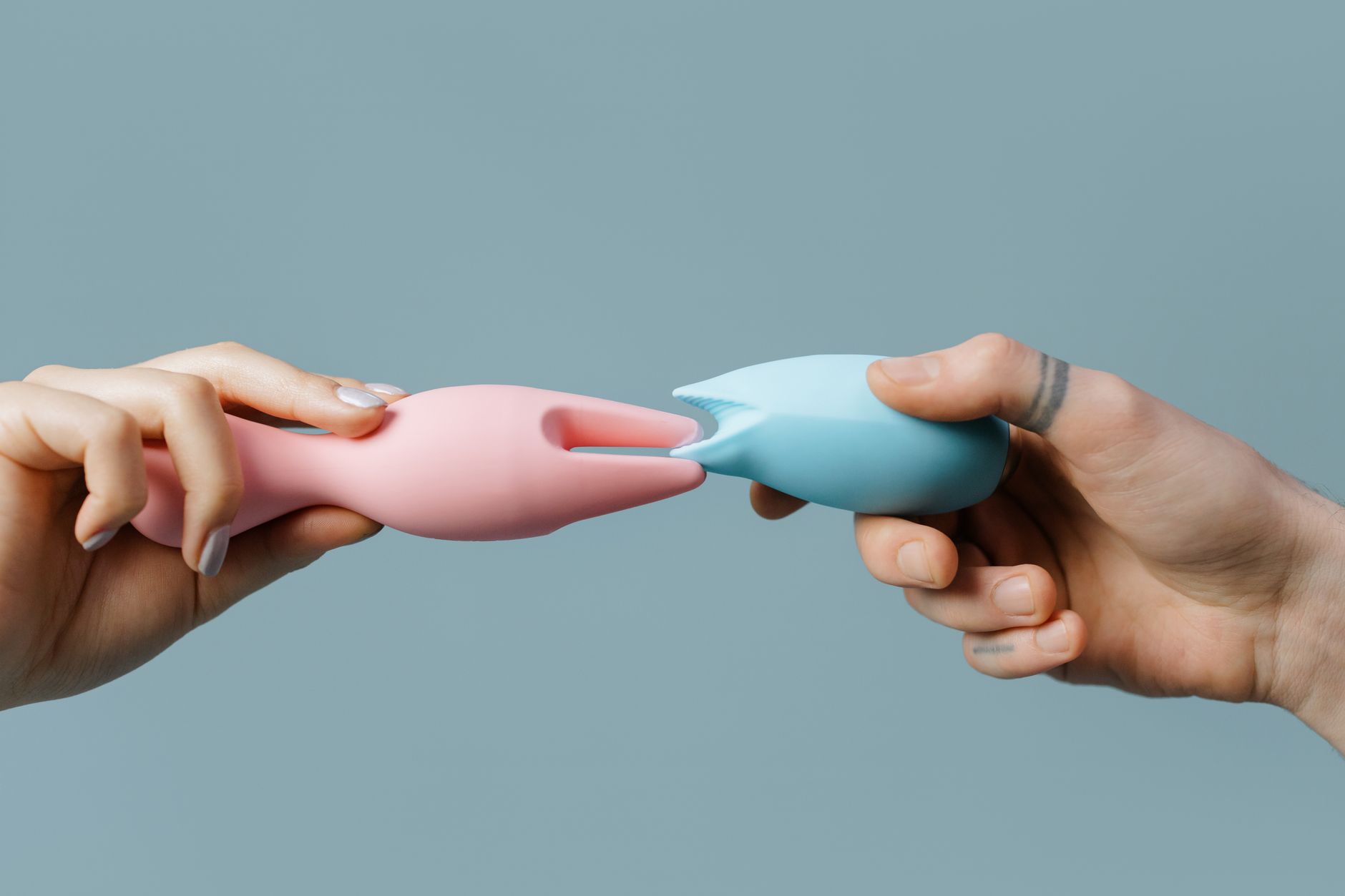 Hands holding blue and pink silicone vibrators in a contemplative manner