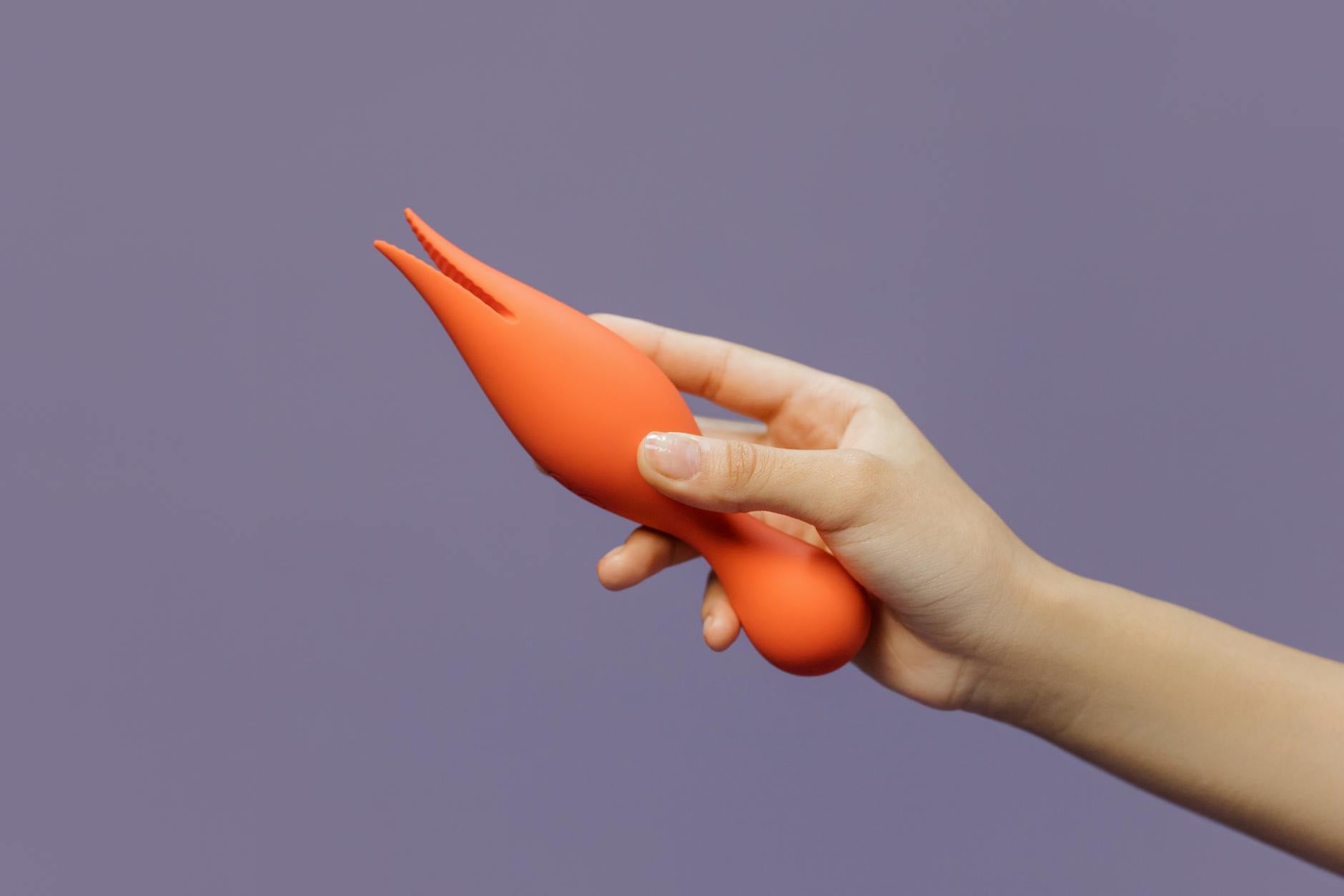 Close-up of a hand holding a yellow lemon vibrator against a minimalistic purple backdrop
