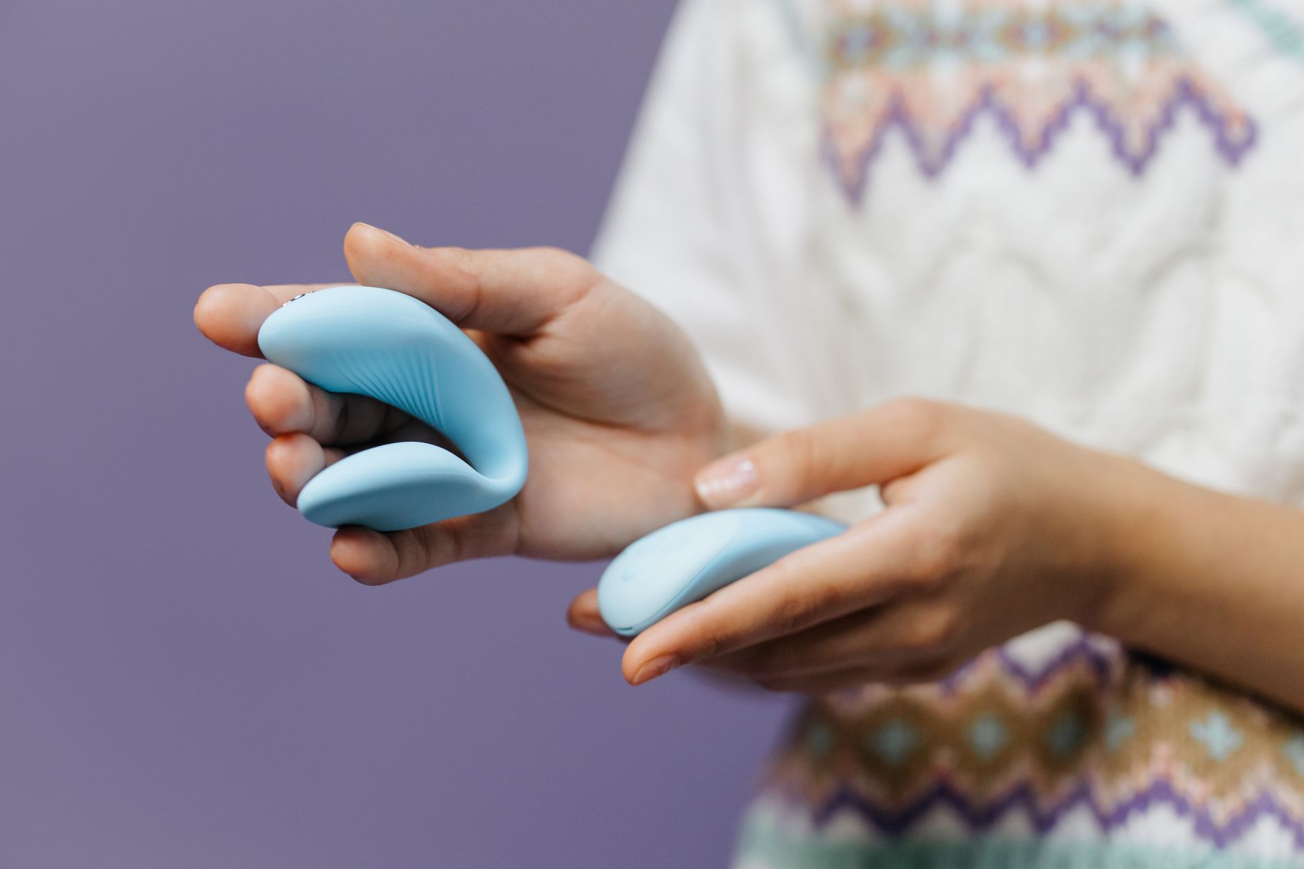 Close-up of hands holding a sleek blue vibrator against a purple background, representing intimate pleasure and self-discovery.