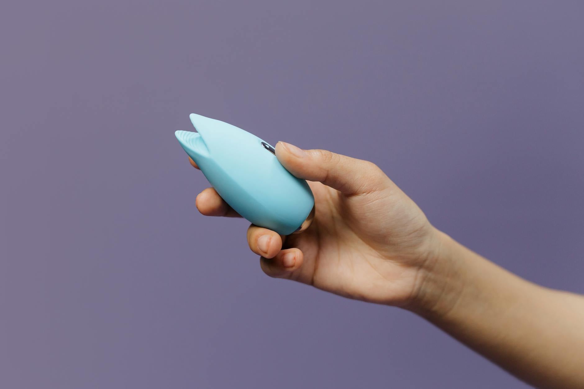 A silicone clitoral vibrator held in hand against a purple background, symbol of self-pleasure and intimacy